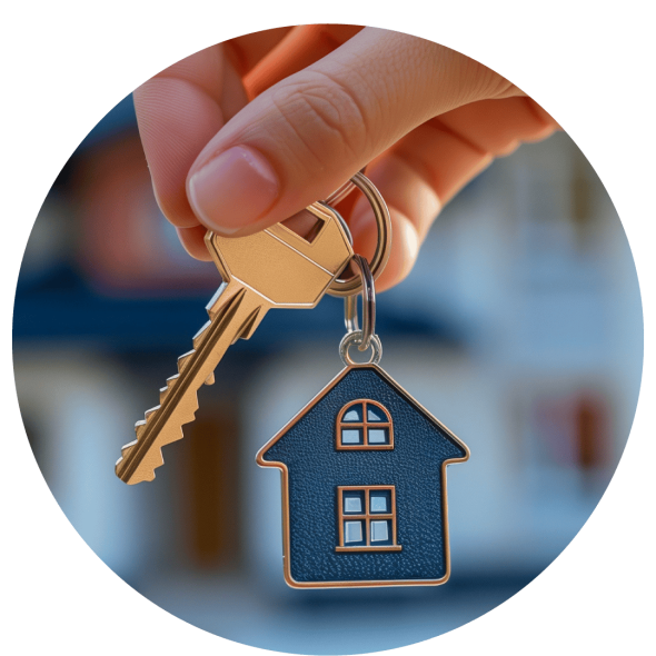 A hand is holding a golden key attached to a keyring with a small house-shaped pendant, and in the background is a well-maintained, two-story home.
