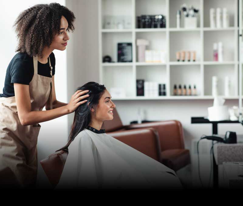 A hairdresser consults with her client while she is seated and wearing a white smock in a well lit salon.